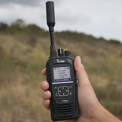 Hand holding Icom SAT 100 radio with a blurred natural background